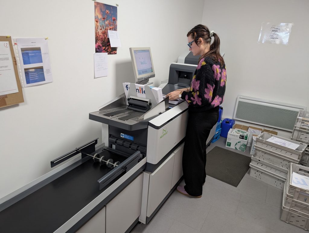 Une employée est à côté d'une machine professionnelle qui imprime et met sous plis pour décrire cette prestation : Lorient routage courrier et impressions.